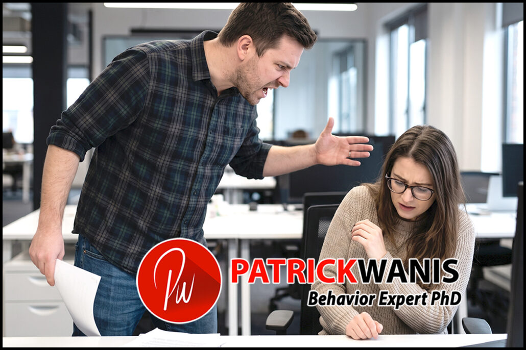 An angry man in a plaid shirt aggressively shouting at a cowering female colleague sitting at her desk in an office environment.